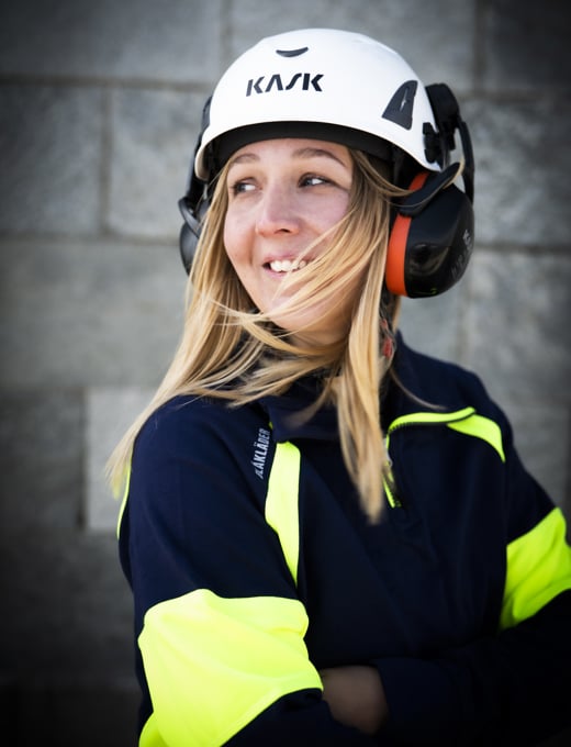 En leende kvinnlig elektriker med armarna i kors över bröstet och en skyddshjälm på huvudet