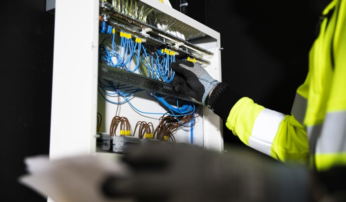 Person i varselväst fixar med något i ett elskåp.