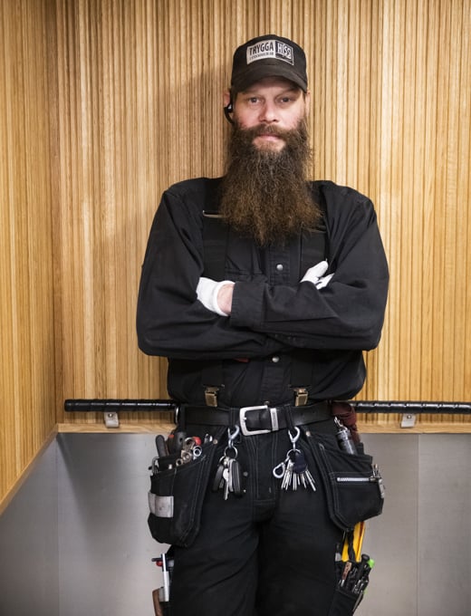 En hissmontör som står i en hiss med armarna i kors över bröstet och ler