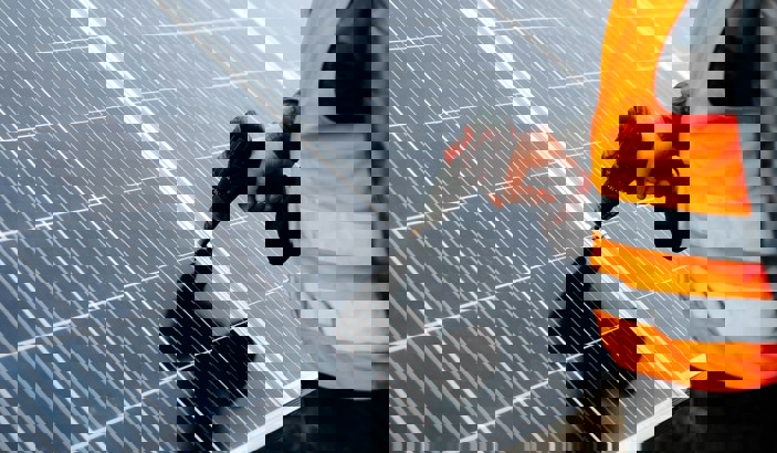 Person i varselväst monterar solcellspaneler med hjälp av skruvdragare.